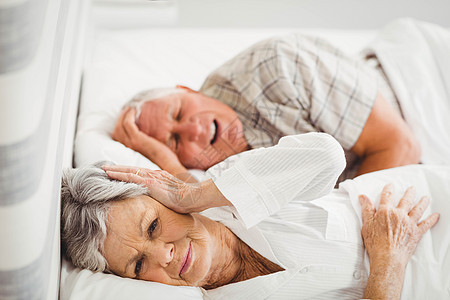 高贵的女子在男人打呼噜的时候 用耳罩着她的耳朵夫妻住所房子睡眠男性老年女性晚礼服退休卧室图片