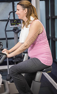 正在骑自行车的孕妇身体女性纺纱腹部微笑闲暇健身室调子护理俱乐部背景图片