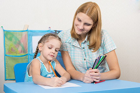 5岁孩子在教师旁边用铅笔的纸纸上画画图片
