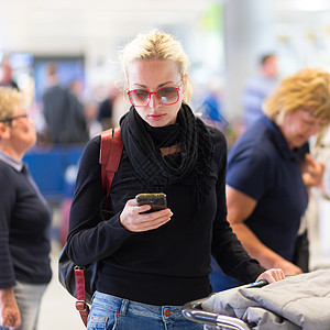 女性旅行者在等待时使用手机上网休息室行李电话公共汽车互联网时间火车手提箱运输图片