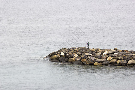 渔夫在石块上用钓竿钓鱼图片