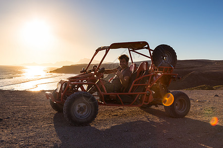 男人在日落时驾驶四重车岩石车辆司机假期海洋乐趣沙漠运输海岸线引擎图片