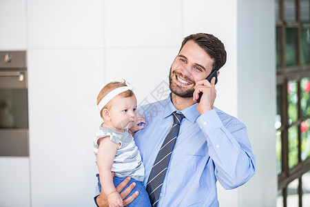 商务人士在带女儿时用手机交谈 女微笑女孩住所技术人士团结父亲婴儿家庭女性图片