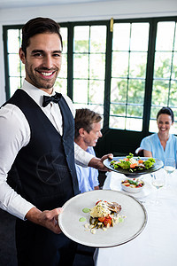 站在顾客旁边吃饭的服务员肖像服务酒店餐厅微笑女士制服款待桌子美食家沙拉图片