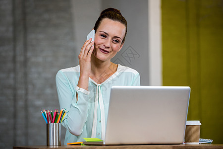 妇女使用笔记本电脑时在移动电话上说话图片