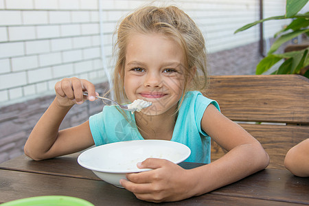 6岁满足在院子里吃饭的六岁女孩 在餐桌边吃粥图片