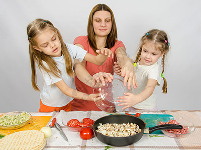 妈妈和两个女儿在厨房餐桌边 带着一盘蘑菇的妈妈 被倒进锅里图片
