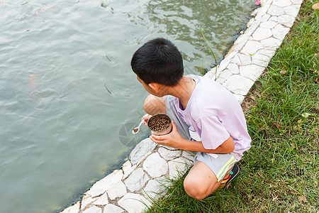 男孩喂鱼勺子衬衫食物池塘孩子生活乐趣童年花园闲暇图片