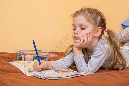 小女孩手里拿着铅笔趴在肚子上 第二只手拿着头 正在研究一本杂志图片
