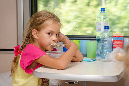 坐在汽车二等舱车厢下层桌子桌边的火车上 一个6岁女孩在车上吃粥勺子和汤匙图片