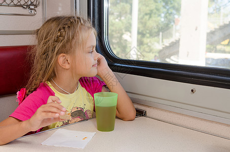 坐在火车上坐着6岁女孩坐在二等车外的桌子上 满腔热情地向窗外看图片