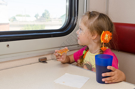 小女孩在火车上的二等车厢外的桌子上喝着三明治喝茶 热情地望着窗外图片