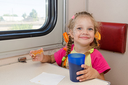 一张笑脸的小女孩在火车外二等车厢的桌子旁喝茶和三明治图片