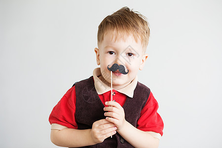一个可爱的小男孩的肖像 带着可笑的纸面胡子冒充乐趣男性微笑金发女郎游戏情感快乐道具工作室图片
