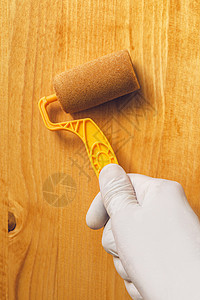 手与油漆滚滚机 在木板上施用丙烯酸男性木头家具涂层黄色硬木工艺男人工具桌子图片