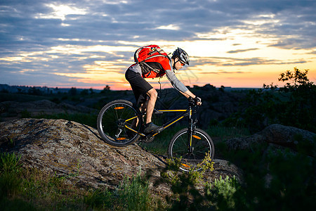 赛车员在日落日落山岩轨上骑乘比克下山丘图片