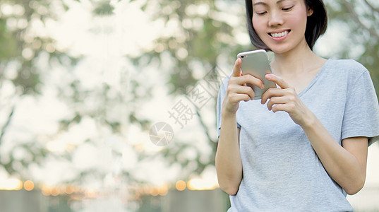 妇女在公园里使用移动智能手机绿色女孩女士电子细胞电话机动性触摸屏手指闲暇图片