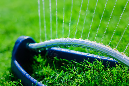草坪喷洒机在绿草上浇水草地生长技术晴天园艺花园水滴喷雾器背光液体图片