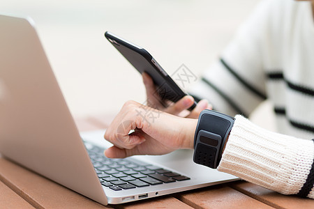 女人把智能手表和手机连接起来笔记本女士软垫手腕同步互联网电话扫描女孩数据图片