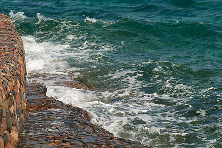 照片显示美丽的绿绿海藻海洋水面表面 在石形海景背景上有波纹和明亮的飞溅 横向图象蓝色晴天海岸线波浪水景流动生态石头液体气氛图片