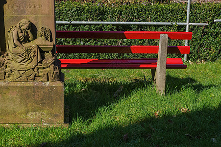 在一座雕像附近木制红色公园长椅的一部分图片