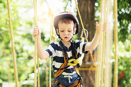 孩子们爬在冒险公园里 男孩喜欢爬绳子木头安全障碍压缩森林头盔金属闲暇绳索幸福图片