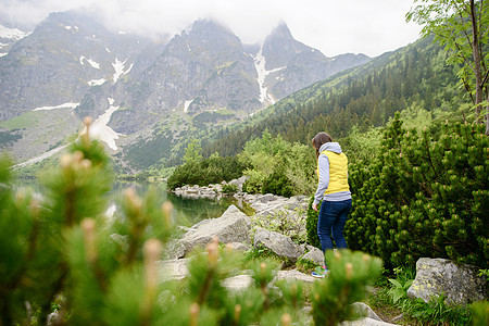 在湖边和山上放松的女士们 阳光明媚的风景远足岩石游客蓝色女孩旅行背包绿色冒险女性图片