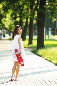 女孩在户外持有塑料滑板街道潮人裙子女士情感长板运动溜冰者青少年青年图片