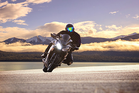 年轻男子骑着大摩托摩托车 与尖锐的灰形曲线相对速度旅行男人游客夹克车辆发动机工程师运动皮革图片