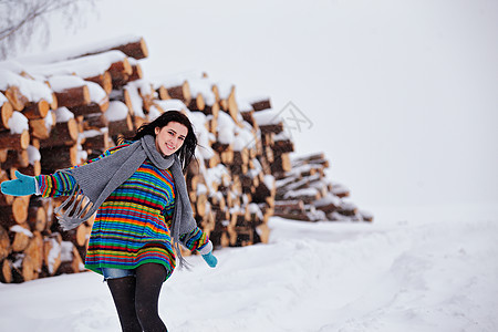 美丽的年轻女子在冬季户外走动木材套衫降雪毛衣手套日志草地围巾女孩松树图片