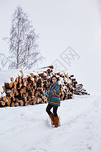 美丽的年轻女子在冬季户外走动降雪微笑女性女孩围巾手套套衫木头长发木材图片