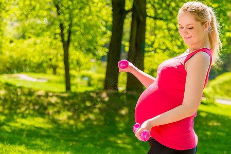 穿粉红色衬衫的孕妇用哑铃做锻炼图片