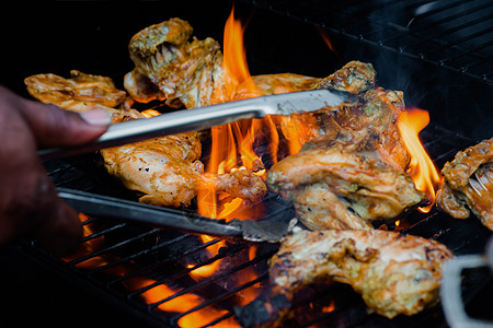 厨师烧烤鸡肉烧烤炉手上的BBQ鸡木炭炙烤烹饪食物车削黑色鸡腿大腿黄色火焰图片
