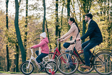 快乐的家庭在公园骑自行车爸爸母亲乐趣闲暇女性男人树木男性父母成人图片