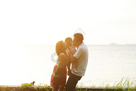 父母在海滩日落时亲吻孩子图片