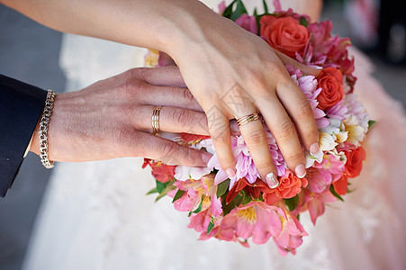 新娘和新郎手与戒指在婚礼花束上图片