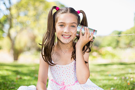 通过锡罐监听的年轻女孩电话农村乐趣玩具服装听力沟通草原微笑晴天公园图片