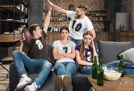 在家支持最喜欢的足球队时 坐在男人兴奋的身边的无聊年轻女子身旁爆米花友谊成人女性手势欢呼啤酒电视朋友们酒精图片
