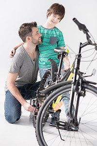 父亲和儿子在检查白色新自行车时拥抱着快乐的父亲和儿子图片