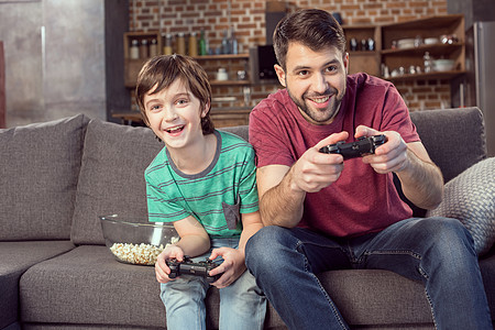 微笑的父亲和儿子在家玩电子游戏图片