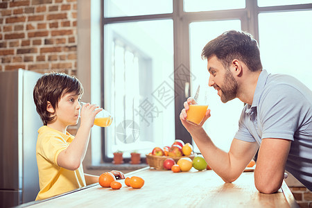 快乐的父亲和儿子一起喝新鲜果汁的侧面风景厨房孩子早餐家庭时代青春期童年饮料爸爸饮食图片
