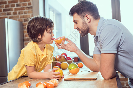 父亲和儿子在厨房吃柑橘水果的侧面观景图片
