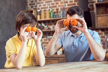 快乐的父亲和儿子在厨房里玩柑橘水果父母时代食物早餐童年少年孩子家庭男生橘子图片