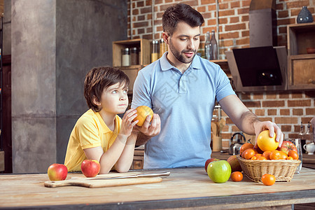 父亲和儿子在厨房餐桌上从篮子中挑选水果图片