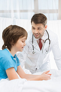 医生看着小男孩病人坐在医院的床上看病时微笑的人图片