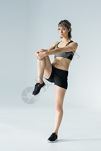 青年女运动员培训和在灰色上伸展腿图片