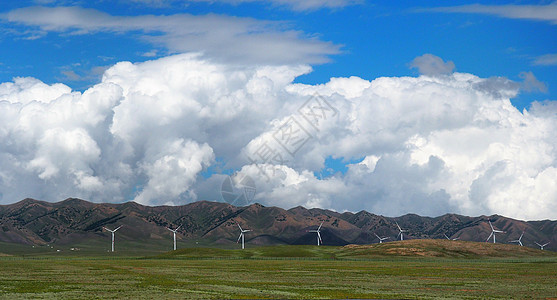 风轮机或绿色草地上的风力涡轮机或风车 有山地云彩蓝天背景图片