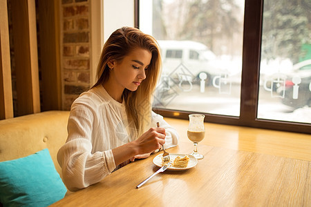 美丽的女孩在吃蛋糕 坐在咖啡厅边笑着笑咖啡早餐店铺微笑酒吧咖啡店时间女性食物杯子图片