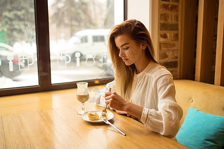 美丽的女孩在吃蛋糕 坐在咖啡厅边笑着笑咖啡店闲暇杯子微笑午餐女士早餐时间食物女性图片