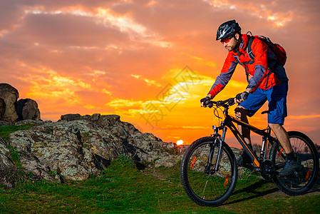 赛车手在美丽的日落山边骑着 极具活力的运动和冒险概念 的自行车下春落雪山踪迹岩石乐趣天空爬坡骑士头盔男人活动山地车图片